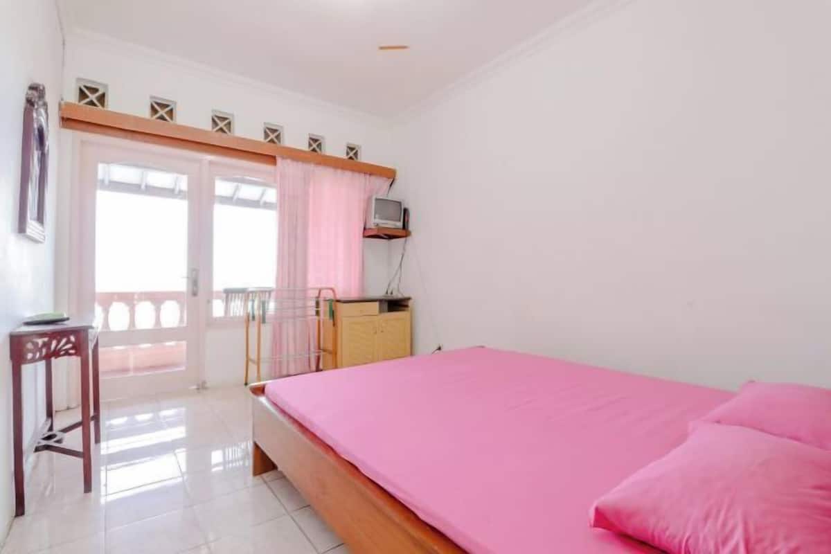 Un dormitorio con cama, escritorio, silla, televisor y balcón.