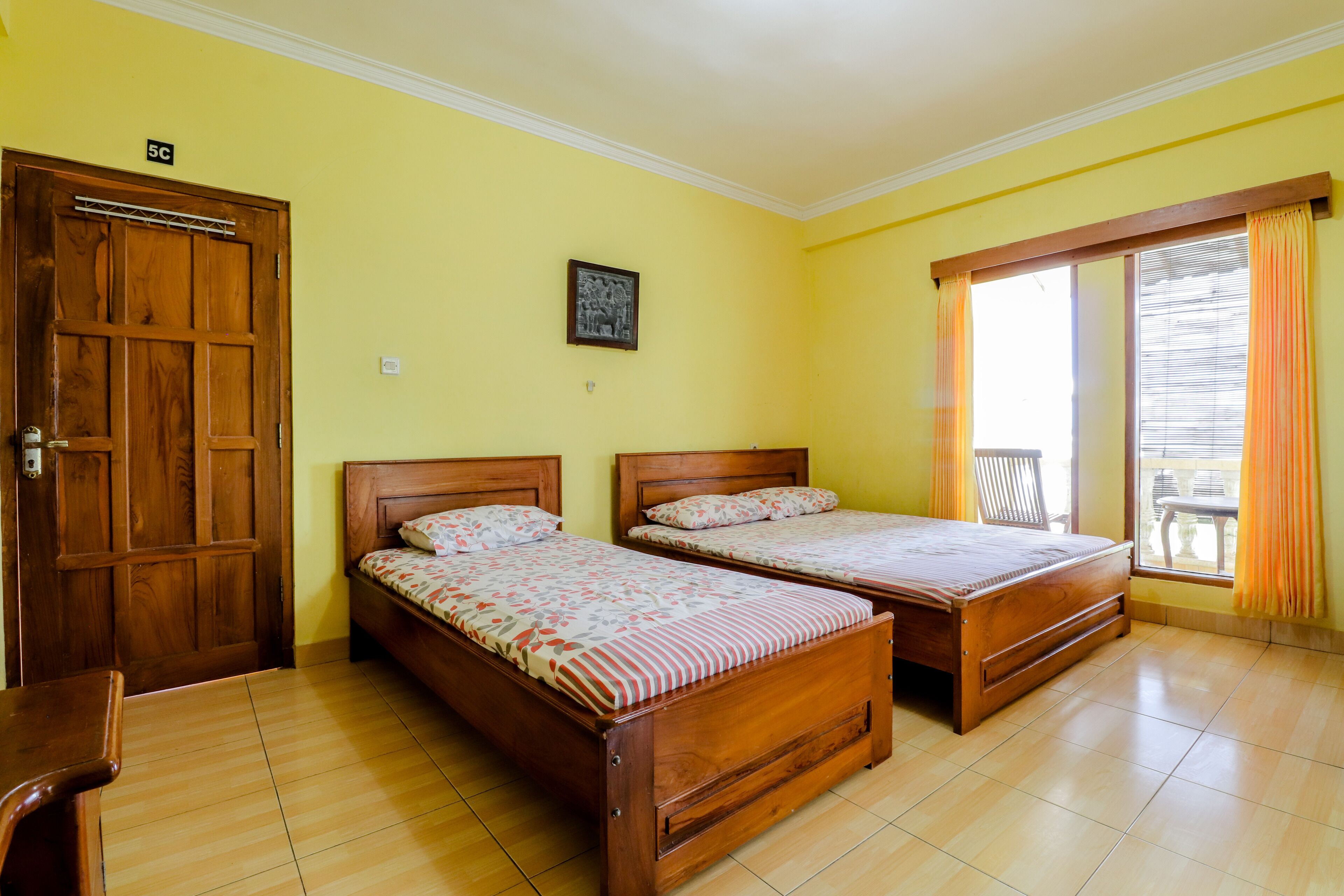 Una stanza con due letti di legno, una porta in legno, un quadro appeso al muro e una finestra con tende.
