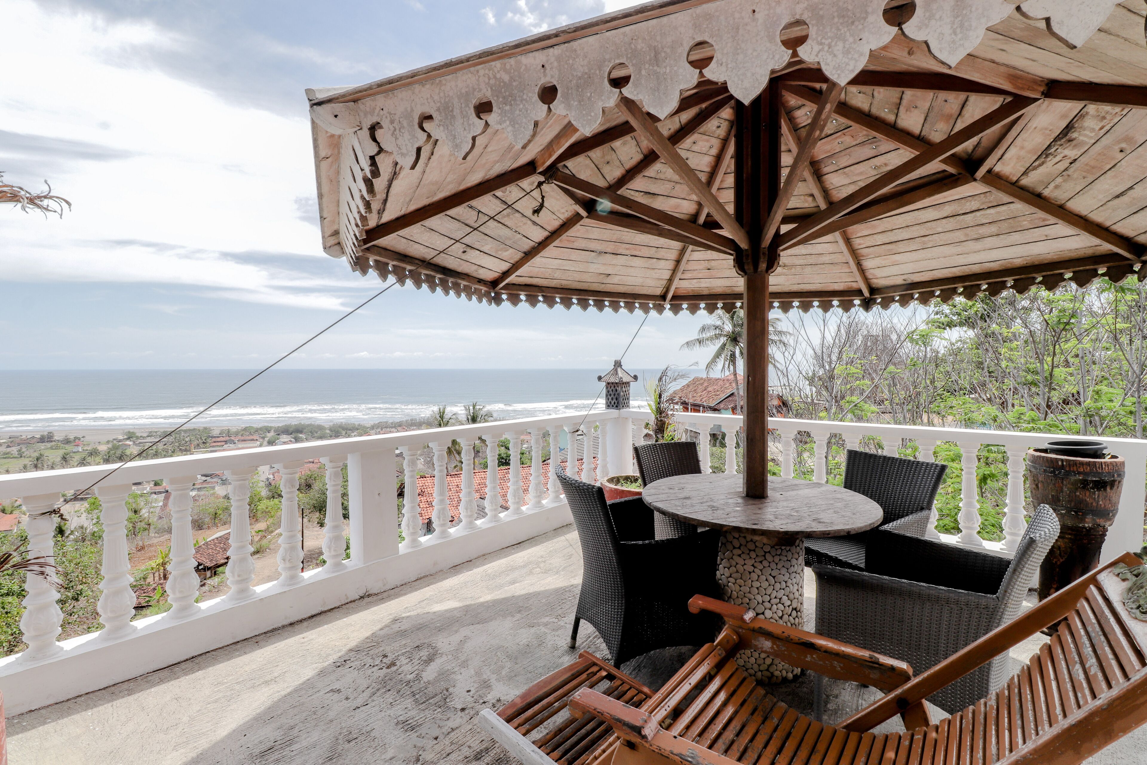 Un balcon avec vue sur l’océan, une table ronde avec des chaises et un grand parasol.