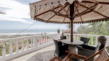 Un balcon avec vue sur l’océan, une table ronde avec des chaises et un grand parasol.