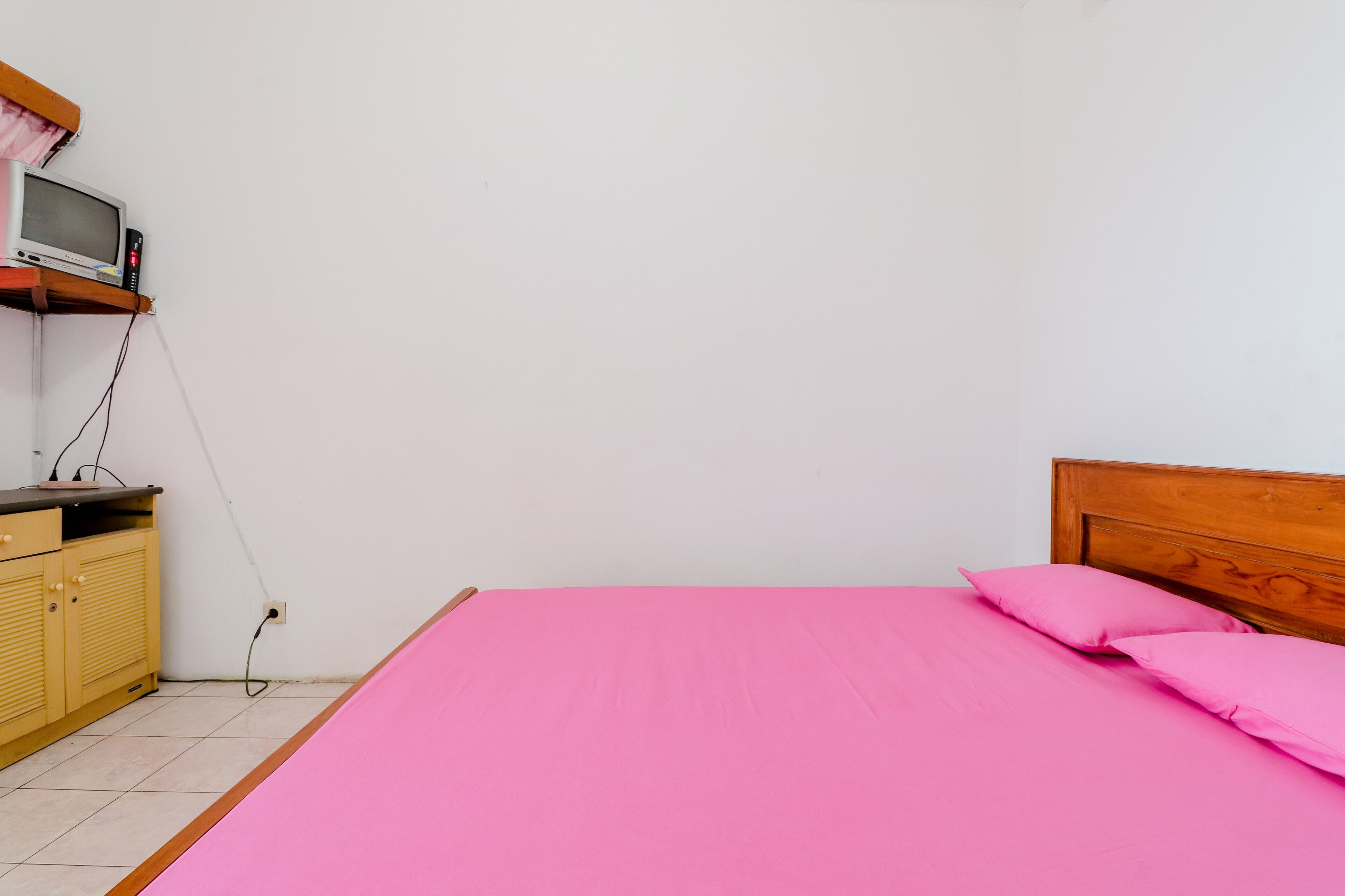 A bedroom with a wooden headboard, a pink bedspread, and a television on a shelf.
