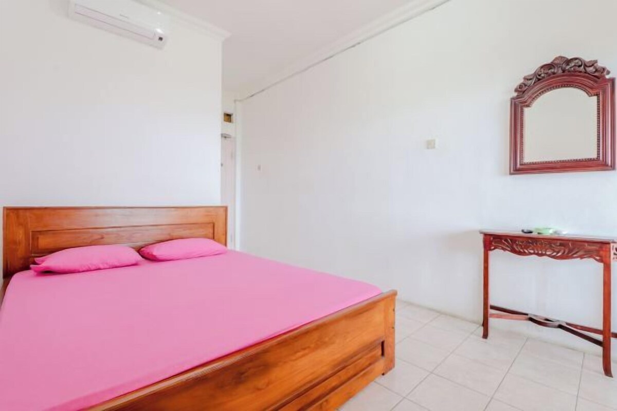 Una habitación con una cama de madera, una mesita de noche, un espejo y una pared blanca.
