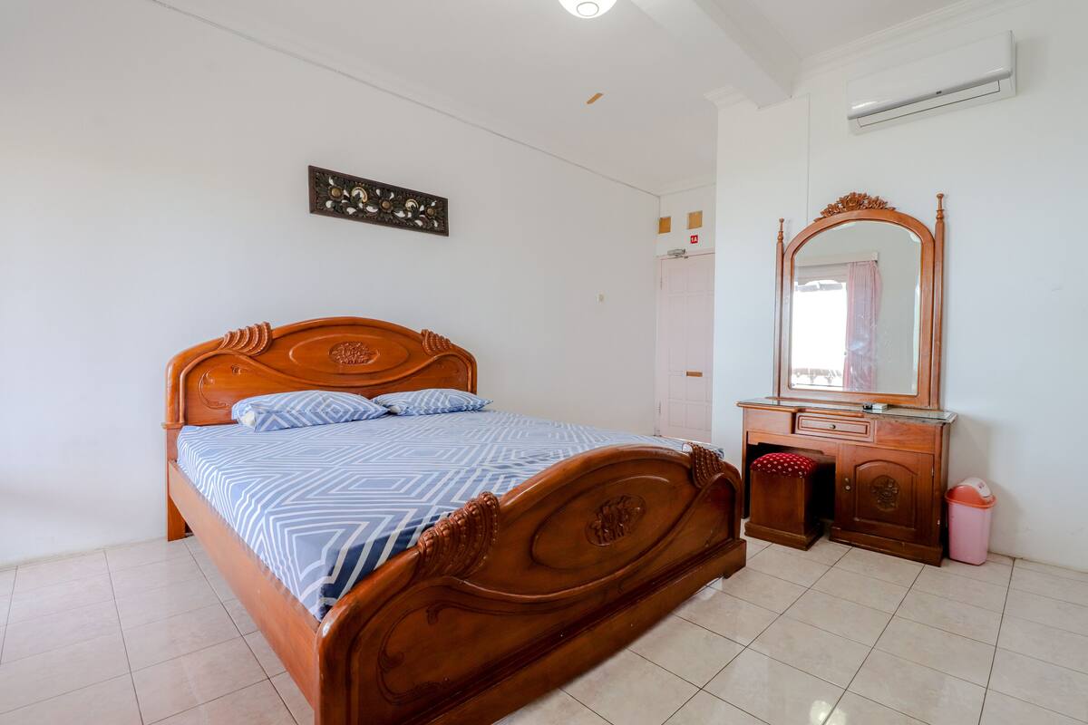 Un dormitorio con una cama de madera, un aparador, un espejo y un aire acondicionado instalado en la pared.