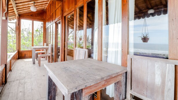 Een houten kamer met een tafel en stoelen, grote ramen en uitzicht op de oceaan.