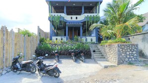 A hostel with a modern design, featuring a central entrance, multiple levels, and a stone wall with plants. - Hostel Bukit Sangcure (Penida Island)