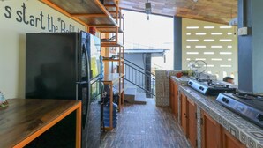 A kitchen with a black refrigerator, wooden shelves, a gas stove, and a staircase leading to an upper level. - Hostel Bukit Sangcure (Penida Island)