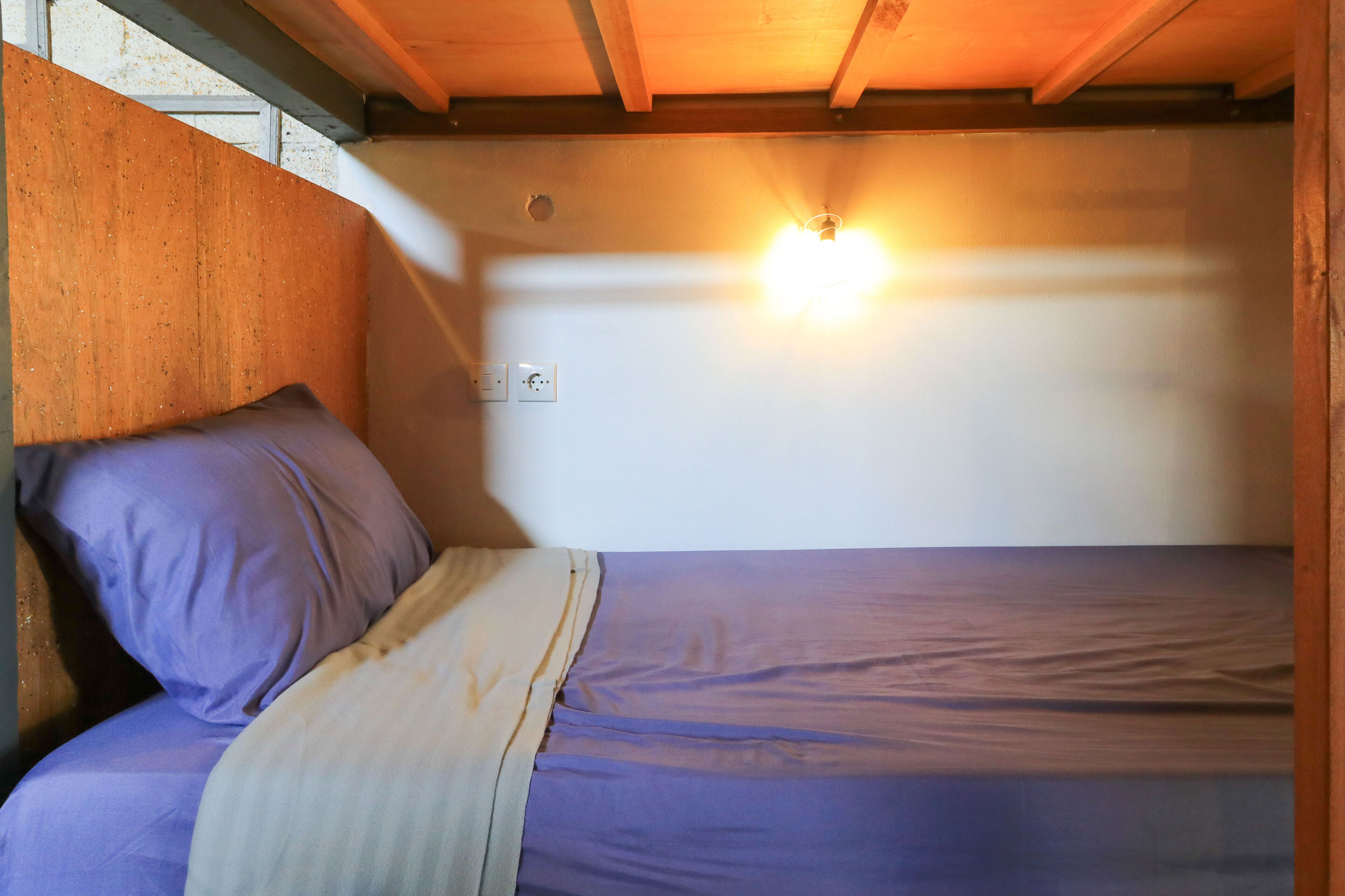 A bunk bed with a headboard, a wall-mounted light, and a power outlet.