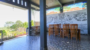 A covered outdoor seating area with a tiled floor, wooden chairs, and a wall with travel-themed drawings and text. - Hostel Bukit Sangcure (Penida Island)