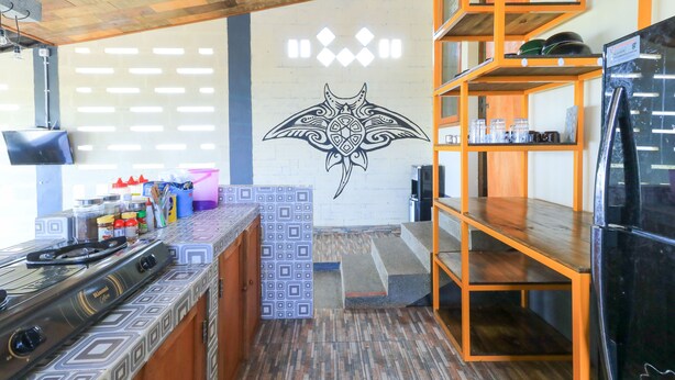 A kitchen with a gas stove, shelves with jars, and a decorative wall mural. - Hostel Bukit Sangcure (Penida Island)