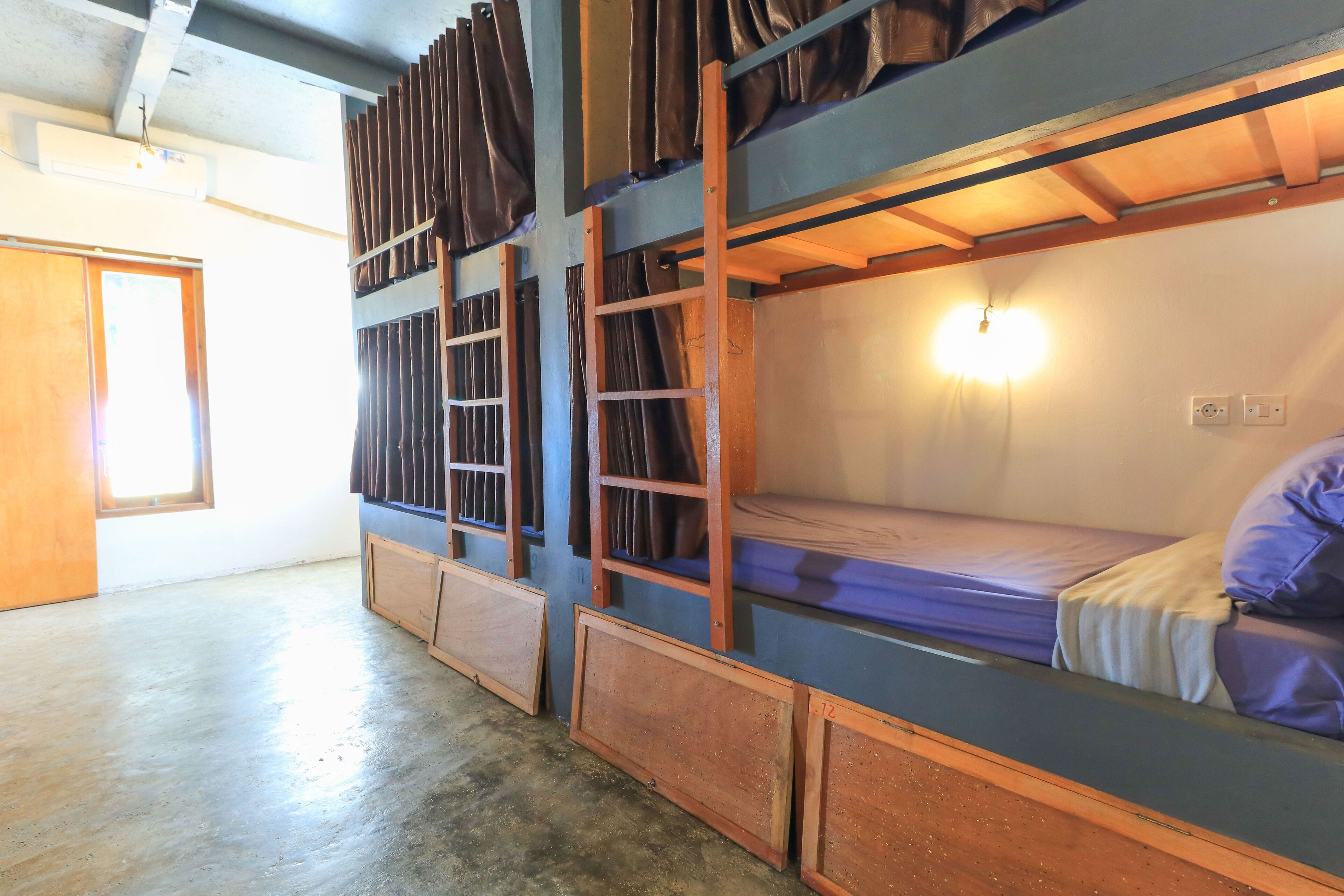 A bunk bed room with a wooden ladder, a window, and a wall-mounted light.