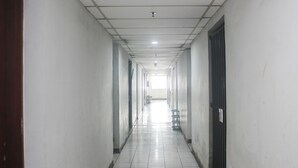A long, narrow hallway with white tiled floors and walls, leading to a bright exit at the end. - Daddy's Room Apartemen City Park (Jakarta)