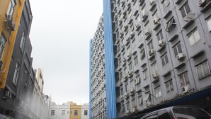 A high-rise building with multiple air conditioning units, a narrow street, and adjacent buildings. - Daddy's Room Apartemen City Park (Jakarta)