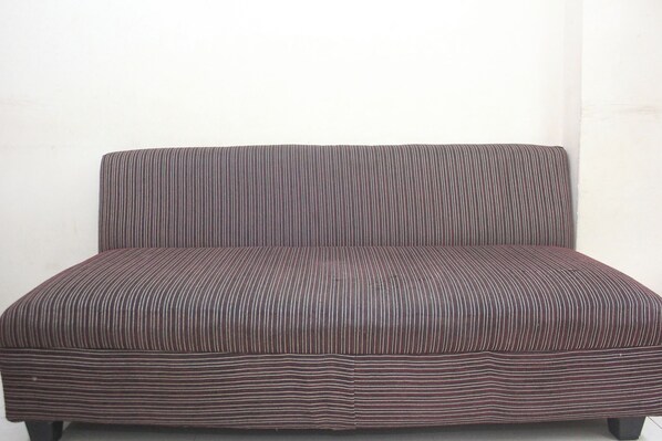 A plain, striped sofa with a high backrest and armrests, positioned against a plain wall. - Daddy's Room Apartemen City Park (Jakarta)