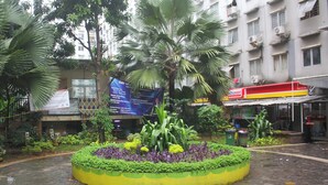 A courtyard with a circular garden bed, palm trees, and a building with multiple air conditioning units. - Daddy's Room Apartemen City Park (Jakarta)