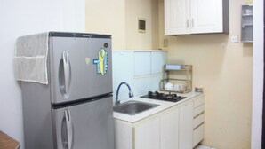 A compact kitchen with a stainless steel refrigerator, a sink, and white cabinets. - Daddy's Room Apartemen City Park (Jakarta)