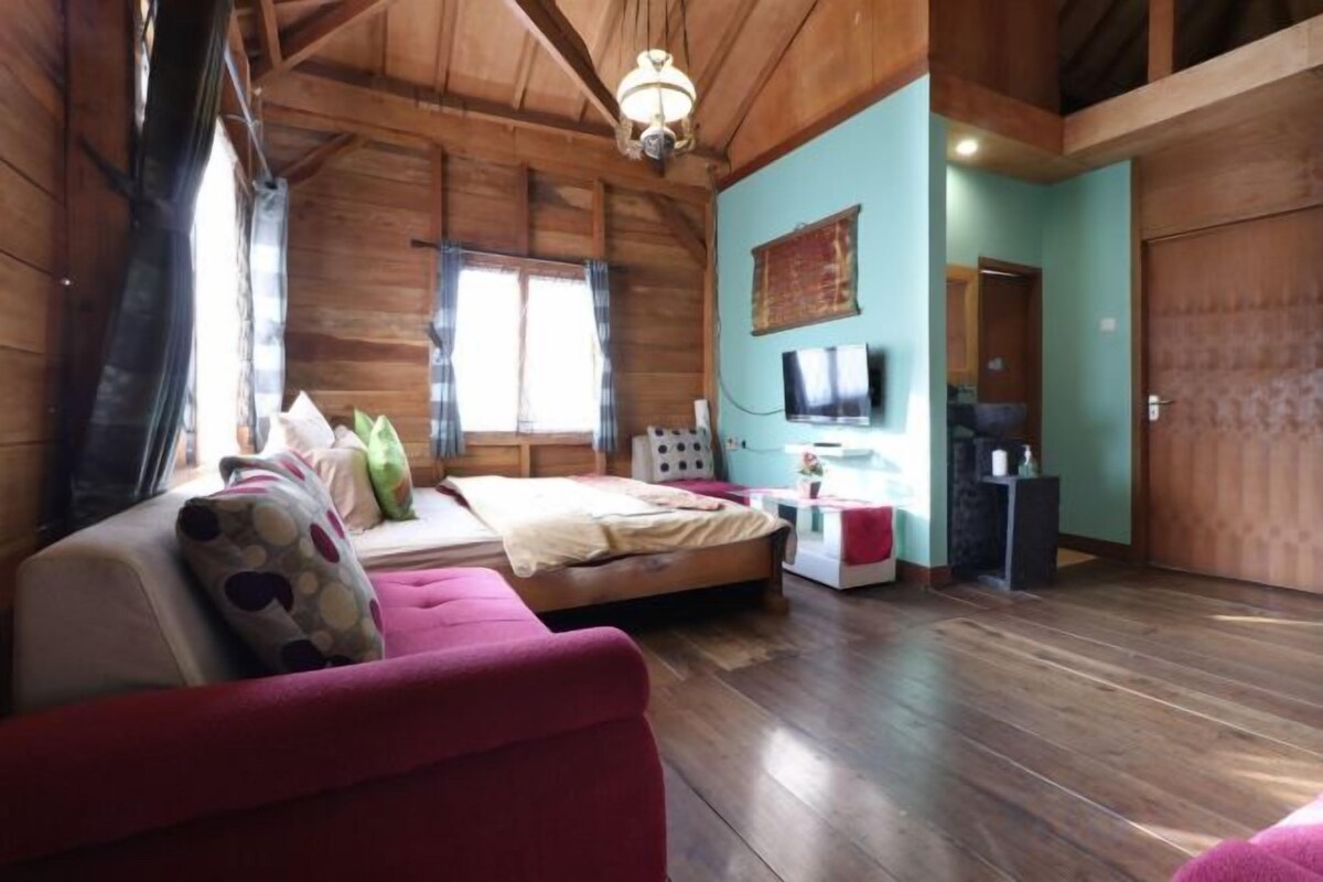 A wooden interior with a bed, a red sofa, a television, and a bathroom with a mirror and sink.