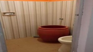 Een kleine badkamer met een toilet, een rode vat en een betegelde vloer.