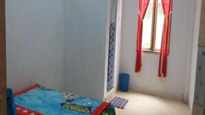 Een kleine, schone kamer met een bed, een raam met rode gordijnen, en een blauwe emmer.