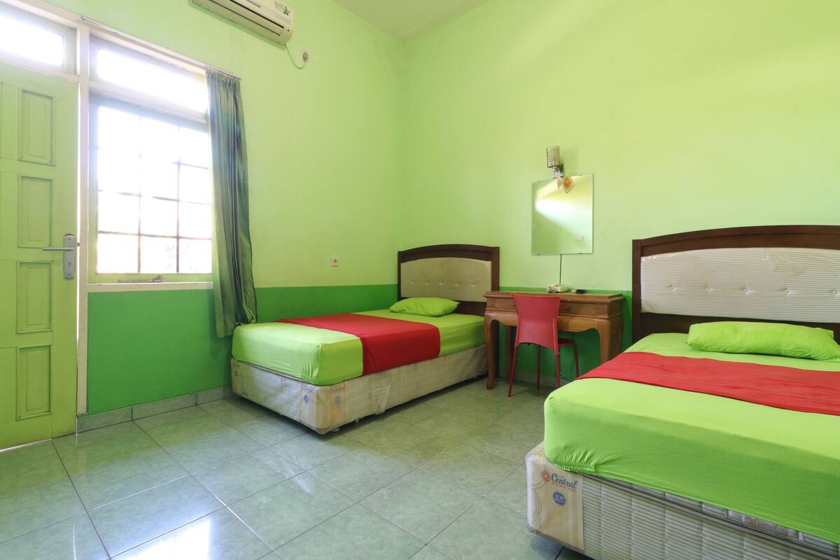 A room with two beds, a desk, a chair, and a window with curtains.