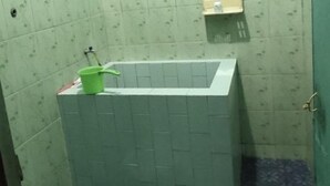 A small bathroom with a toilet, a green cleaning bucket, and a white sink. - Mas Bangkrenx Homestay (Depok)