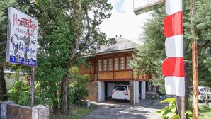 Een traditioneel houten huis met garage, omgeven door groen en een rood-wit gestreepte paal.