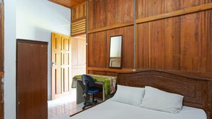 Een slaapkamer met een houten hoofdbord, een bed met witte beddengoed, een bureau met een stoel en een spiegel aan de muur.