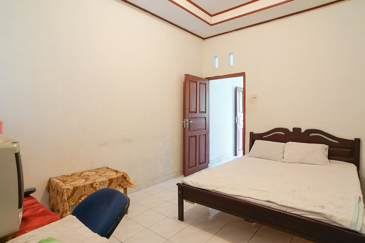 Un dormitorio con cama, una silla, una mesita y una puerta que da a otra habitación.