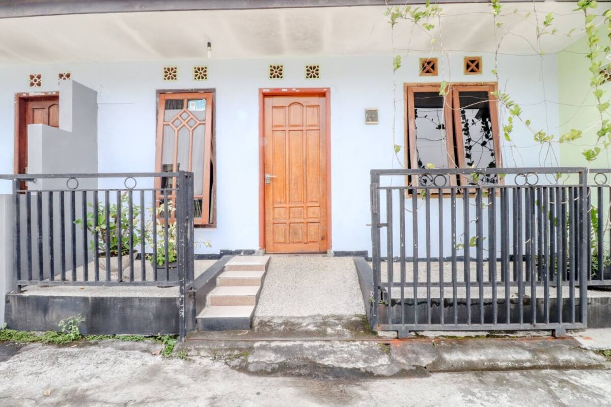 A two-story house with a wooden front door, a small porch, and a metal gate.