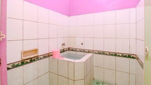 A bathroom with white tiles, a pink wall, and a corner bathtub. - Puspa Sari Villa and Homestay (Batu)