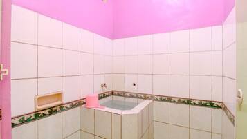 Un baño con baldosas blancas, pared rosa y bañera en esquina.