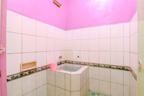 A bathroom with white tiles, a pink wall, and a corner bathtub.