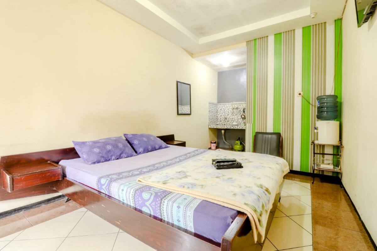 A room with a bed, a chair, a nightstand, a water dispenser, and a mirror.