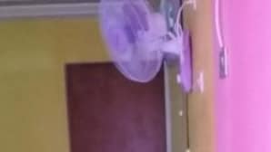 Um corredor com uma porta fechada, um ventilador na parede e chão de azulejos.