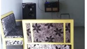 Um quarto com cama, escrivaninha, cadeira, televisão e ventoinha.