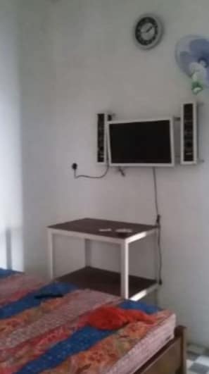 Quarto com cama, escrivaninha e televisão na parede.