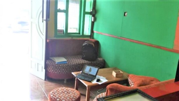A room with a patterned sofa, a small table with a laptop, and a green wall. - Caisar Homestay (Sidoarjo)