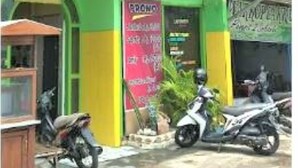 A building with a green and pink facade, a visible sign for 'CAISAR', and two motorcycles parked in front. - Caisar Homestay (Sidoarjo)