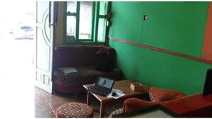 A room with a green wall, a sofa, a small table with a laptop, and a patterned ottoman. - Caisar Homestay (Sidoarjo)