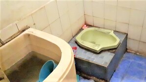 A small bathroom with a bathtub, a toilet, and a blue bucket. - Caisar Homestay (Sidoarjo)