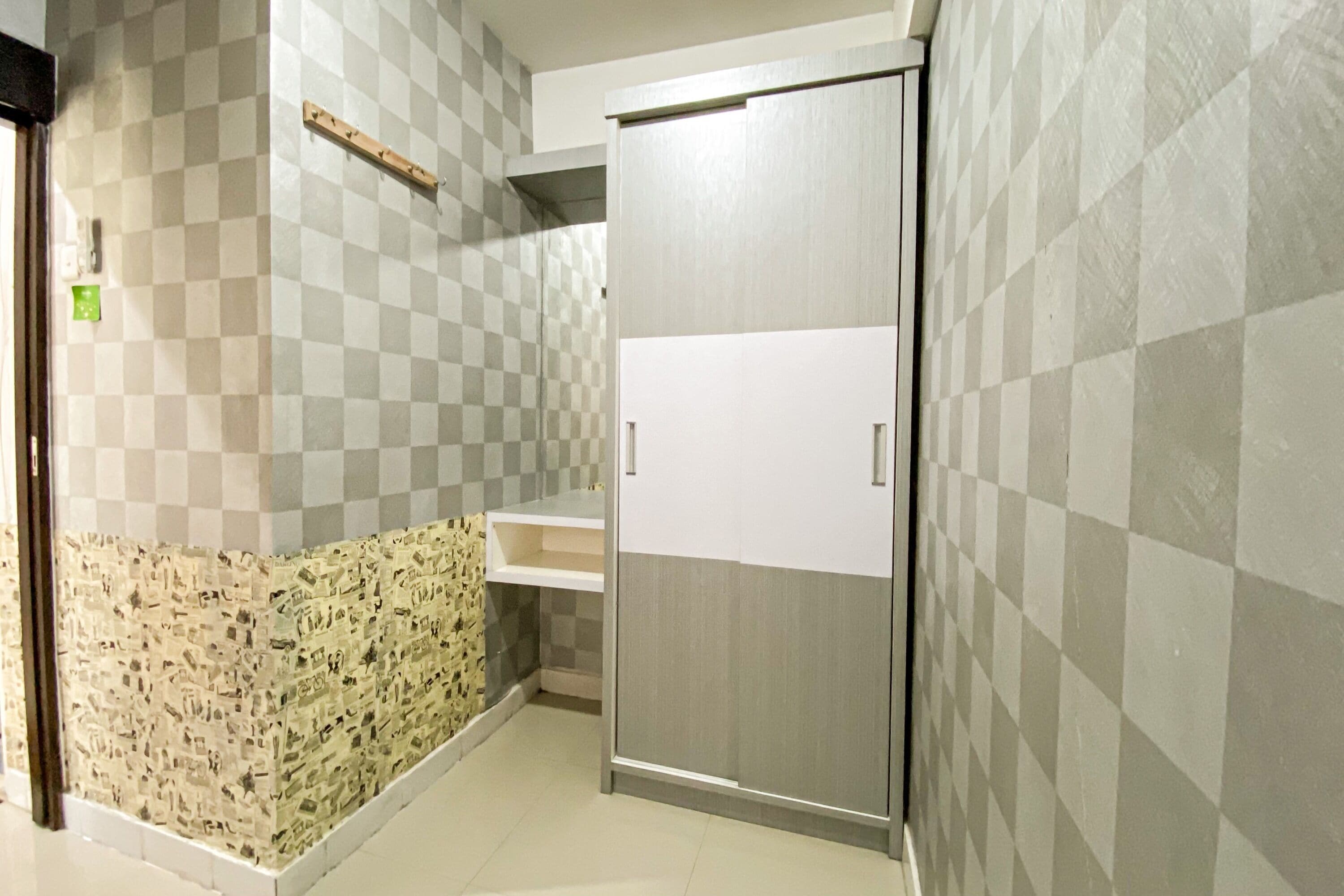 A hotel room with a checkered wall pattern, a wooden shelf, and a wardrobe.