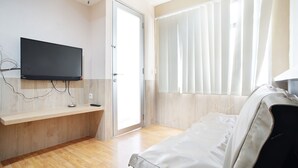 A modern room with a flat-screen TV mounted on the wall, a wooden floor, a sofa, and a window with blinds. - The Jarrdin Apartment by Tempat Singgah (Bandung)