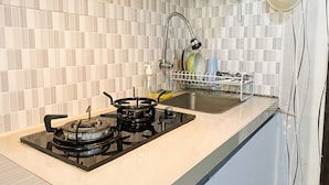 A kitchen with a gas stove, sink, and tiled backsplash. - The Jarrdin Apartment by Tempat Singgah (Bandung)