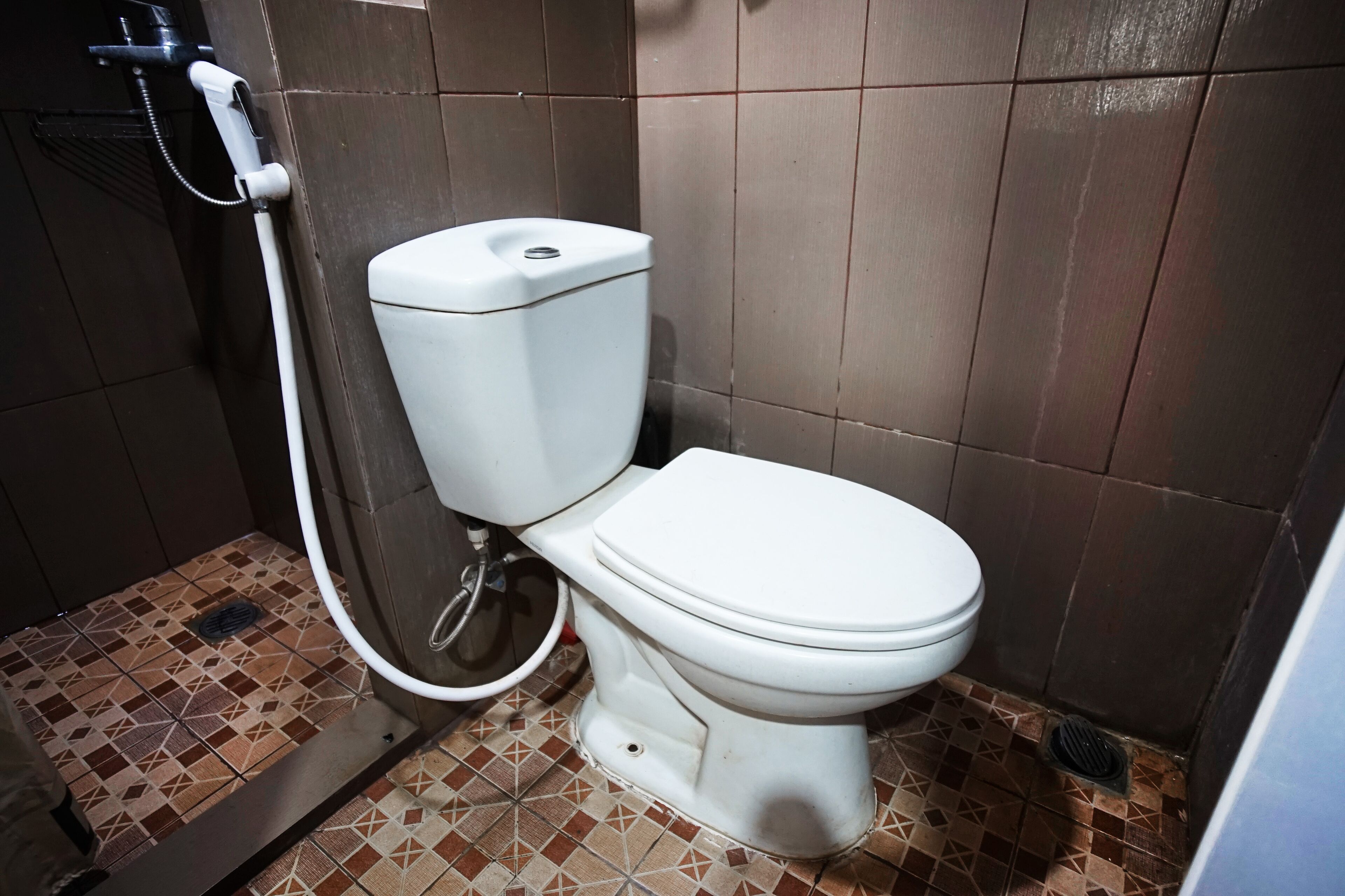 A toilet with a bidet attachment in a bathroom with patterned tile flooring.