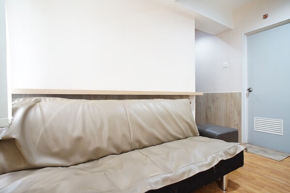 Una habitación moderna con un sofá beige, un pequeño otoman gris y piso de madera.