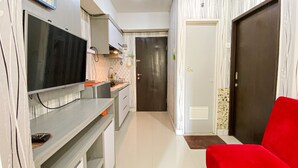 A modern kitchen with a flat-screen TV, a sink, and a red chair. - The Jarrdin Apartment by Tempat Singgah (Bandung)
