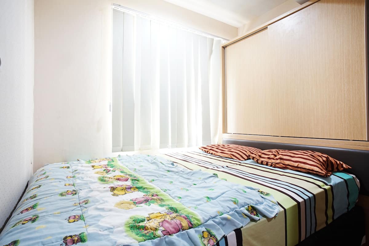 A bedroom with a bed, a window with curtains, and a wooden wardrobe.