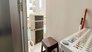A balcony with an air conditioning unit, a small stool, and a storage rack with various items. - The Jarrdin Apartment by Tempat Singgah (Bandung)