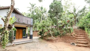 A house with a dirt driveway, a wooden door, and a small porch.