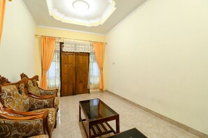 A living room with a sofa set, a glass-top coffee table, and a wooden door with curtains. - Jemakir Homestay (Kokap)