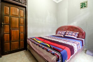 A bedroom with a wooden door, a bed with a colorful bedspread, and a small green decorative item on the wall.
